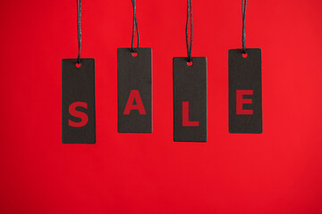 Photo of hanging black price tags on isolated red background with text sale