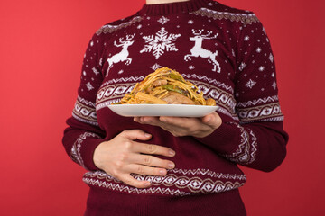 Cropped closeup photo of woman in red and white christmas sweater holding large plate of food and...
