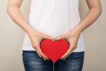 Cropped closeup photo of girl in white t-shirt and jeans holding red paper heart near crotch on...