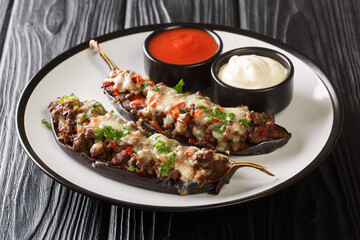 Portion of eggplant stuffed with meat, vegetables and baked with cheese served with sauces close-up in a plate on the table. horizontal