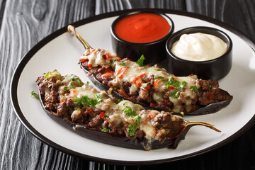 Delicious eggplant stuffed with ground beef, vegetables and baked with cheese, served with sauces close-up in a plate on the table. horizontal
