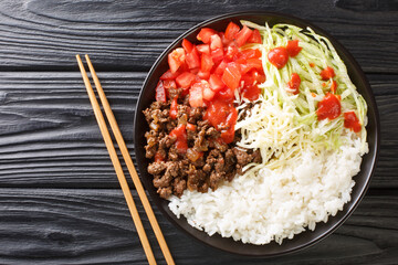 Taco rice takoraisu is a Mexican Japanese fusion dish consisting of seasoned ground beef, shredded lettuce, and chopped tomatoes served over a bed of white rice close-up in a bowl. Horizontal top view