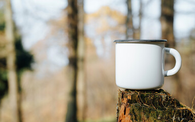Empty metal hiking mug mock-up standing on tree stump in woods outdoors, copy space. Blank new...