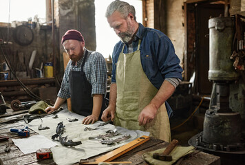 Two colleagues standing near the table with tools and making details together in the workshop