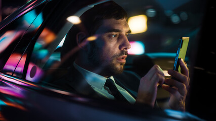 Handsome Businessman in a Suit Commuting from Office in a Backseat of His Luxury Car at Night....