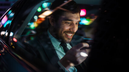 Businessman in a Suit Commuting from Office in a Backseat of His Car at Night. Entrepreneur Playing...