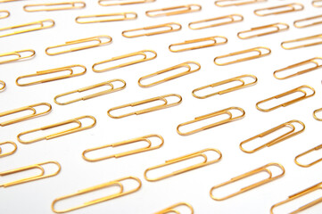 Repeated gold paper clips on the white background. Paper clips pattern, minimal creative concept.