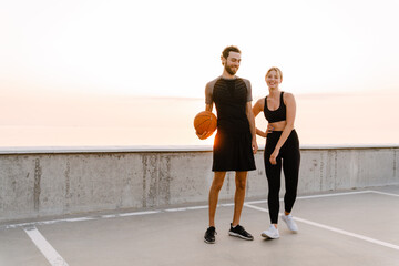 Young man and woman working out with ball together on parking