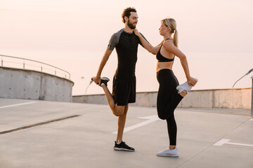 Obraz premium Young man and woman doing exercise while working out together on parking