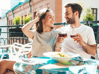 Smiling beautiful woman and her handsome boyfriend. Happy cheerful family. Couple cheering with glasses of red wine at their date in restaurant. They drinking alcohol at veranda cafe in the street