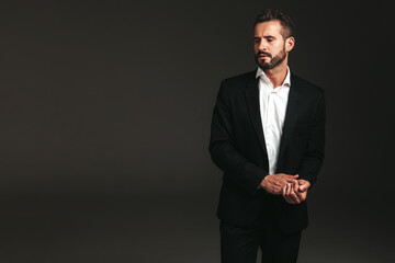 portrait of handsome confident stylish hipster lambersexual model. Sexy modern man dressed in elegant black suit. Fashion male posing in studio on dark background