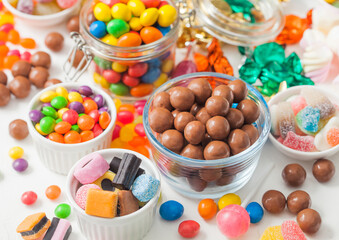 Milk chocolate candies in shell with jelly sugar gums and liquorice allsorts and fruit sherbet candies on white with marshmallows and strawberry bon bons.