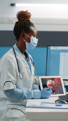 African american medic and patient looking at virus animation on digital tablet while wearing face masks for protection. Black doctor explaining bacteria and disease of coronavirus for woman