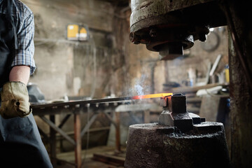 Close-up of man holding metallic stick and forging detail from iron during his work in blacksmith...
