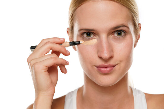 Young blond woman applying concealer under her eyes