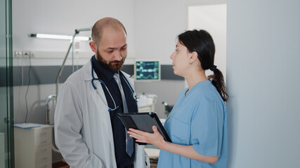 Doctor and nurse with tablet talking about treatment for patient with disease in hospital ward bed. Medical specialists using device for healthcare and recovery in intensive care space