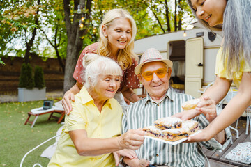 Man and women eating cakes while having picnic by trailer