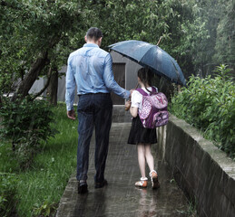 The father leads the child to school in the rain. A manifestation of sacrificial love
