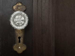 Close-up photo of a clear glass doorknob on an old rusted metal plate with a skeleton keyhole on a brown weathered wooden door. Copy Space.