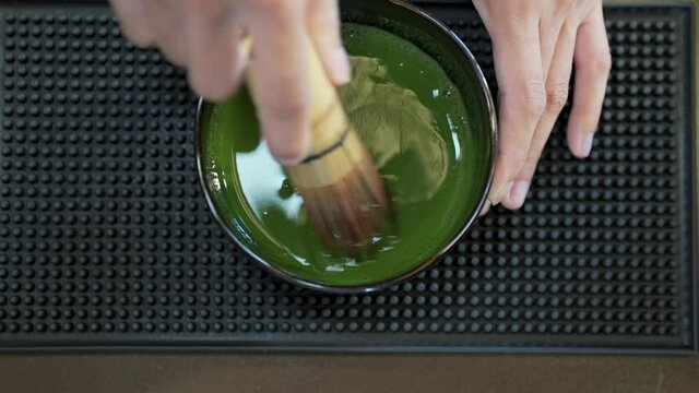 4K Asian woman barista making green tea with fresh milk in the glass. Female coffee shop waitress serving iced matcha latte to customer on counter at cafe. Small business coffee shop owner concept.