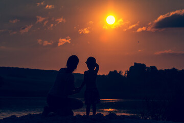 Fototapeta na wymiar woman and child on sunset background over summer river.