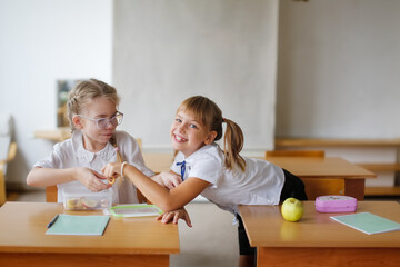 Two girlfriends of classmate at school have snack at desk.Kid takes food from friend's lunchbox. Pranks and hide and seek, kids at school. Funny school days, friendship children during their studies