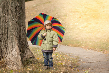 Obraz premium Little boy hiding behind colorful umbrella outdoors