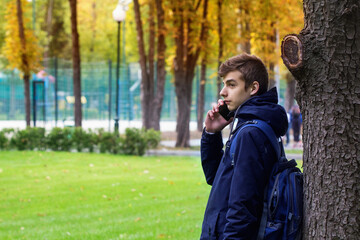 Portrait of Teenager guy with a smartphone talking phone. Park outdoor.