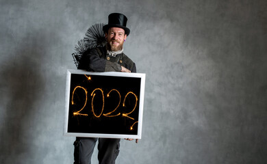 Schornsteinfeger in Arbeitskleidung mit Bilderrahmen und Jahreszahlen 2022, strahlend geschrieben...
