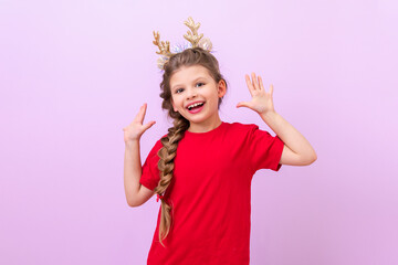 A little girl in a festive New Year's horns on her head is very happy and shows her palms. On a purple isolated background.