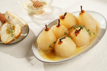Peeled poached pears with caramel sauce on a white oval plate on a white table surface