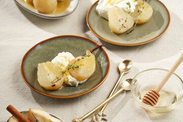 Caramelized pear halves with whipped cream on an green plates with thyme branches and caramel on a linen cloth