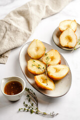 Caramelized pear halves on an oval grey plate with thyme branches and caramel on a white table surface