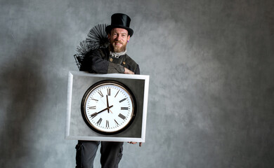 Kaminfeger in Arbeitskleidung und mit Kehrgeräten, hält Bilderrahmen mit Bild einer großen Uhr.