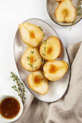 Caramelized pear halves on an oval grey plate with thyme branches and caramel on a white table surface