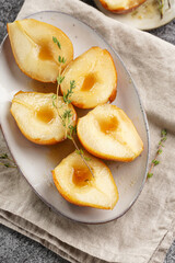 Caramelized pear halves on an oval grey plate with thyme branches and caramel on a linen cloth