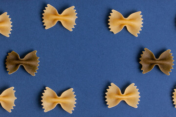 Pattern made of uncooked farfalle pasta on dark navy background. Macaroni background. Top view, flat lay. 