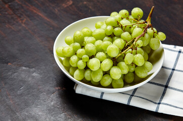 Branch of ripe green grape on plate with water drops. Juicy grapes on wooden background, closeup. Grapes on dark kitchen table with copy space