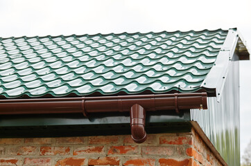 Facade of a suburban building with downspout. View of the roof against the sky
