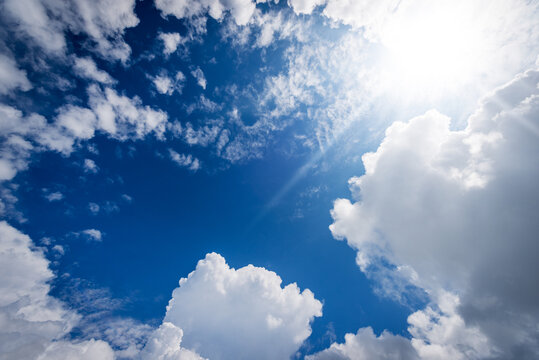 Beautiful blue sky with white cumulus clouds and sun rays (sunbeams). Backlight photography.