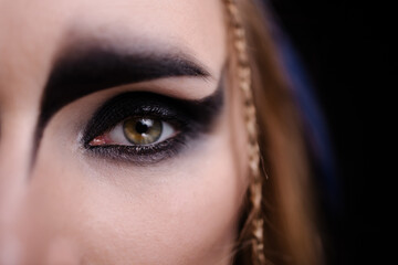 Close-up of eyes with Halloween makeup. Celtic goddess harpy costume smokey eye. Carnival banner. Copy space black background. Magical witch. Macro eyes and make-up. - obrazy, fototapety, plakaty