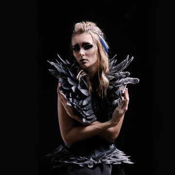 Beautiful woman in makeup and costume for halloween on a black background. Fantasy image of a harpy or valkyrie. Celtic mythology character. Wings and feathers. Smokey eyes. Carnival girl black bird