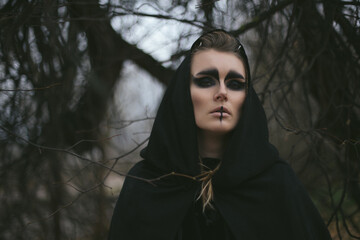portrait of a witch in a hood and a cloak in the forest. Halloween mystical atmosphere. Celtic...