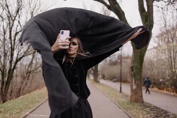 A woman in a witch costume is talking on a video call. Online holiday. Masquerade in autumn outside...