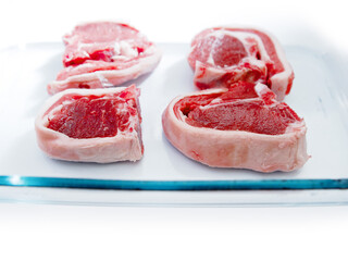 Obraz premium Four fresh uncooked lamb loin chops in a glass tray ready to cook, on white background. Selective focus. Meat industry product. Rich red color of the meat