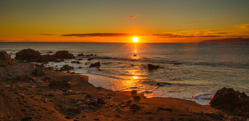 Fototapeta na wymiar The rugged wild coastline at Cape Palliser with a magnificent vibrant sunset on the horizon