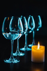 burning candles and glass goblets on a black background. bright candles and graceful glasses of wine on the dining table. glasses with white wine and candles