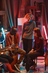 Young people singing while their friend playing guitar during party at home