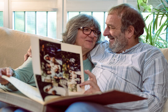 Elder couple reminiscing their past, happy seniors looking at their wedding book together