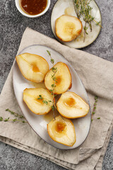 Caramelized pear halves on an oval grey plate with thyme branches and caramel on a linen cloth